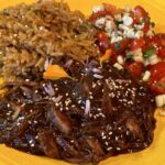 Photo shows Shredded Turkey with Molé Rojo along with Mexican Rice and Corn Salsa on a bright yellow plate