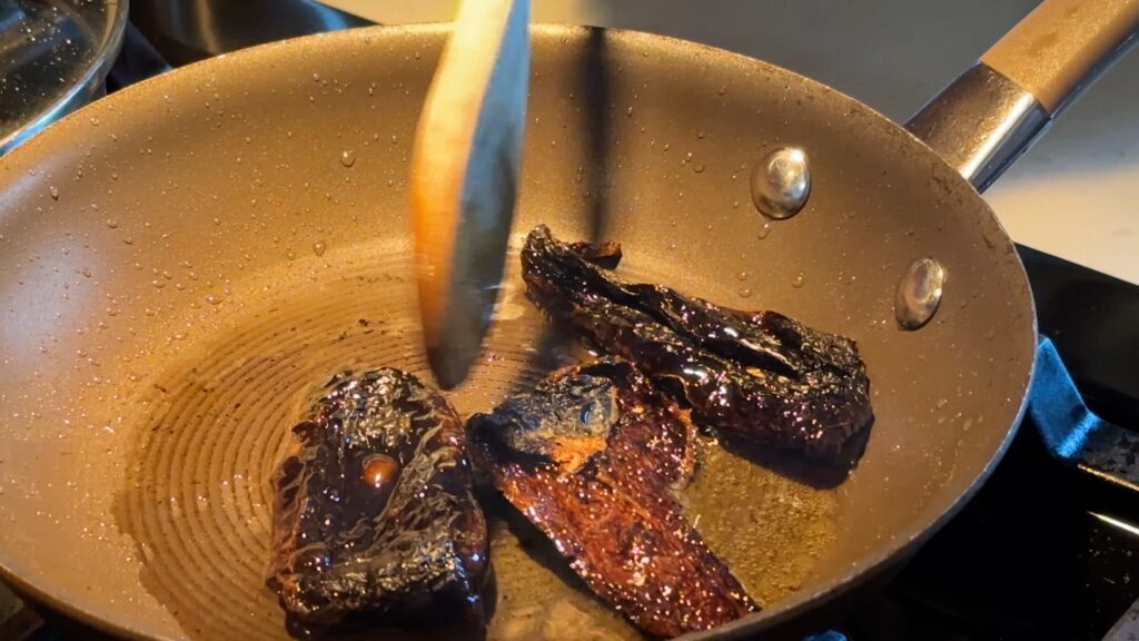 Pieces of ancho chile in the hot oil. One clearly has a blister from cooking