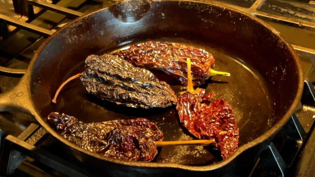 Photo shows whole dried chiles sweating in a cast iron pan