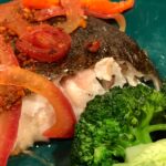 Photo shows fish plated with broccoli, tomato and pink onion.
