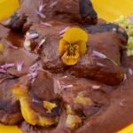 Photo shows a plate with Chicken, corn and tostones covered with a dark molé.