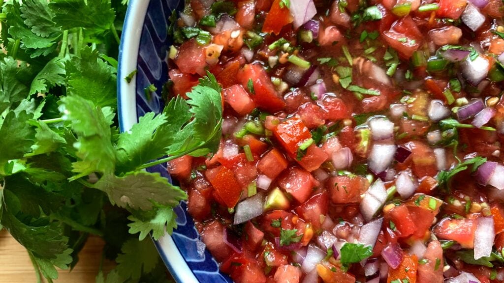 Photo shows a bowl of salsa with cilantro on the side.
