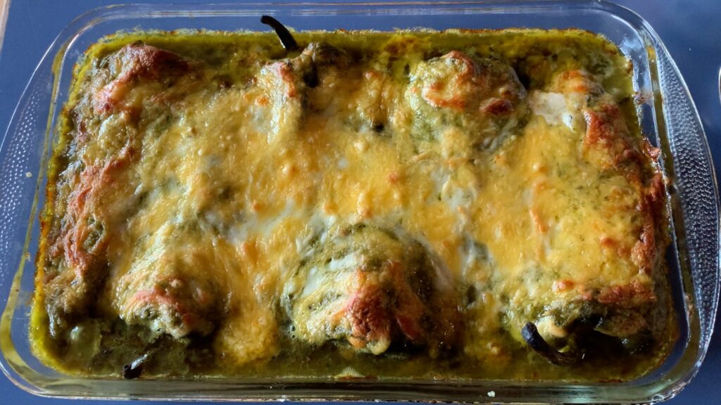 Image shows stuffed poblanos in a pan smothered with Poblano Sauce