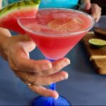 Photo shows a red drink in a large martini glass with a watermelon garnish