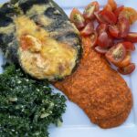 Photo shows stuffed poblano pepper plated with Roasted Red Pepper Sauce, tomatoes and kale salad