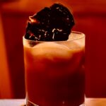 Photo shows the reddish brown holé molé cocktail with an out of focus wood background