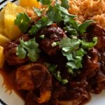 Photo shows Camarones a la Diabla, a thick dark sauce with shrimp, plated with Mexican Rice and Pineapple.