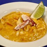 Photo shows a bowl of yellow curry crab with a slice of fresh lime
