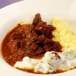 Photo shows a bowl of lamb curry served with rice and raita