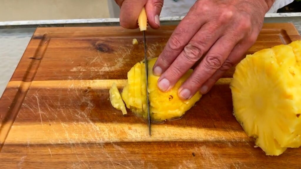 Photo shows making thin cuts through a stack of pineapple
