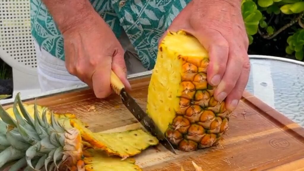 Photo shows the skin being cut off the pineapple