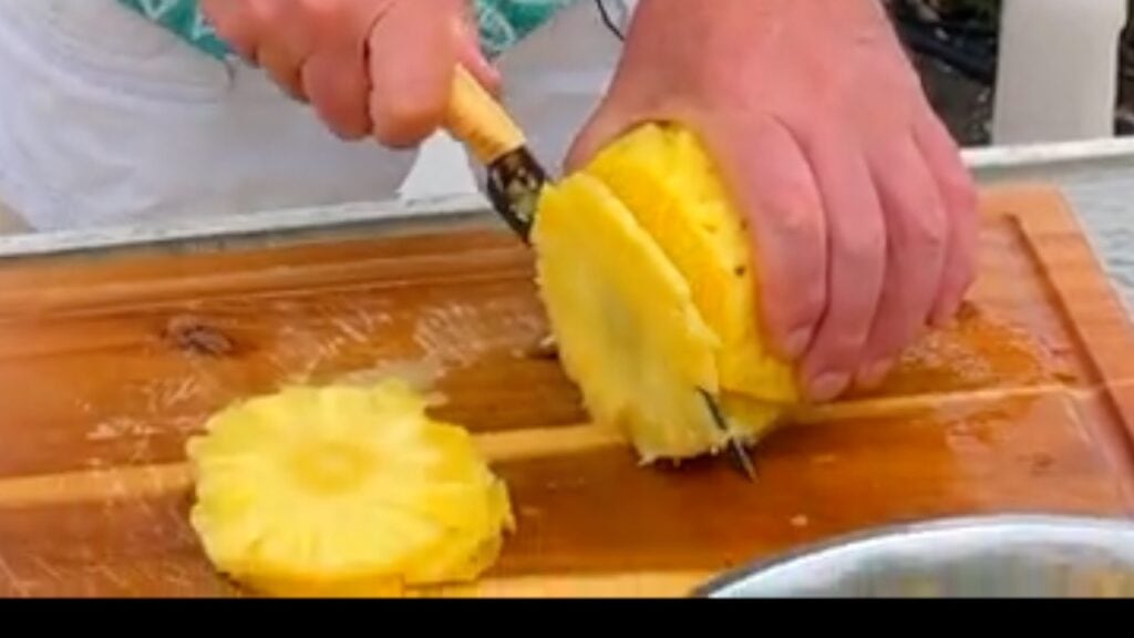 Photo shows taking thin slices off the width of the pineapple