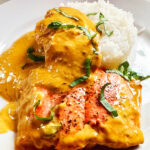 Photo shows Red Curry Salmon plated with rice and basil garnish.