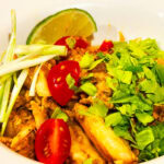 Photo shows a bowl of curry garnished with cherry tomato, celery leaves, sliced green onion and a lime wedge