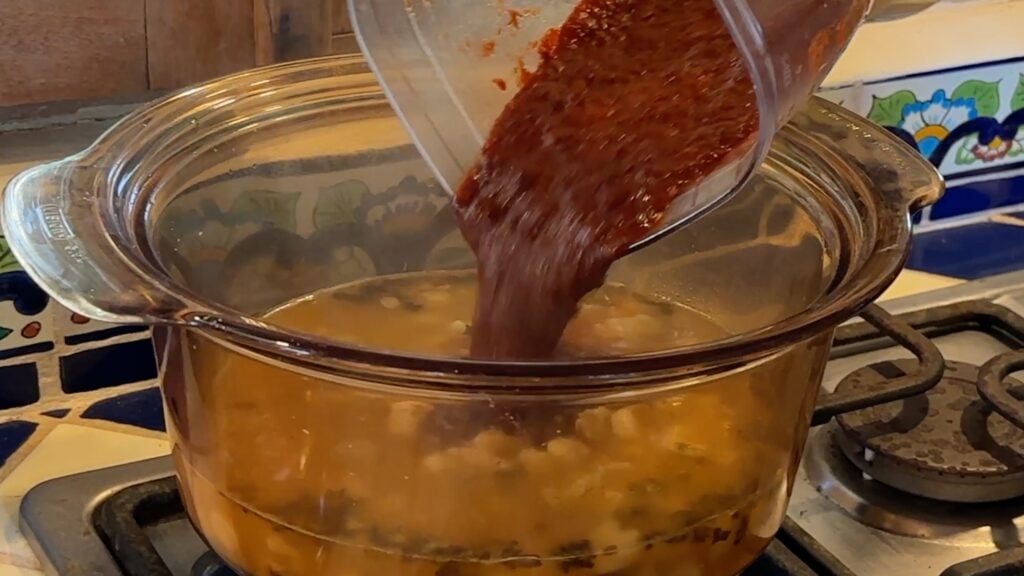 Photo shows the chile mixture being added to the chicken broth and hominy