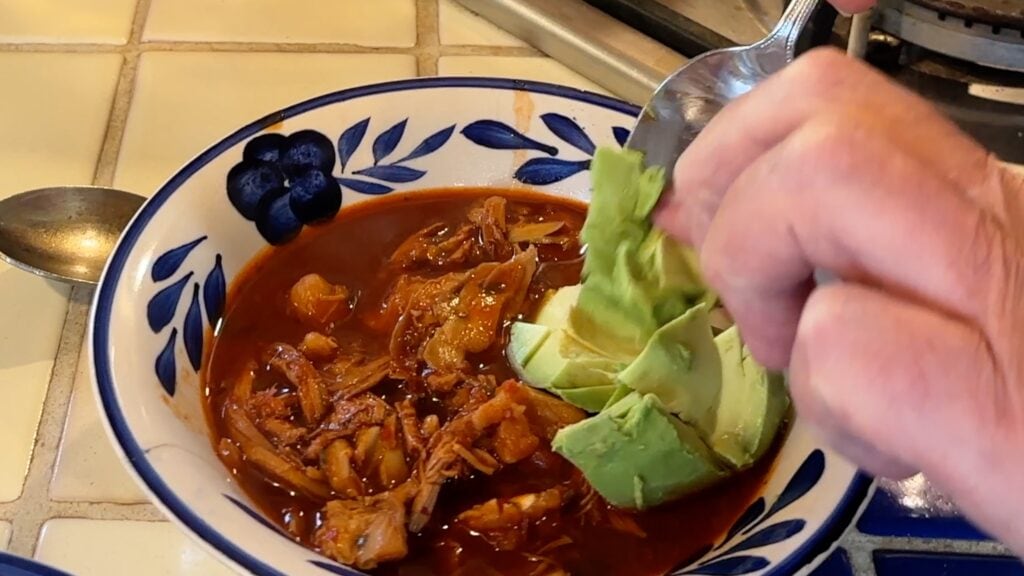 Photo shows avocado being added to the pozole