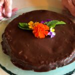 Photo shows the completed chocolate cranberry fudge cake decorated with edible flowers